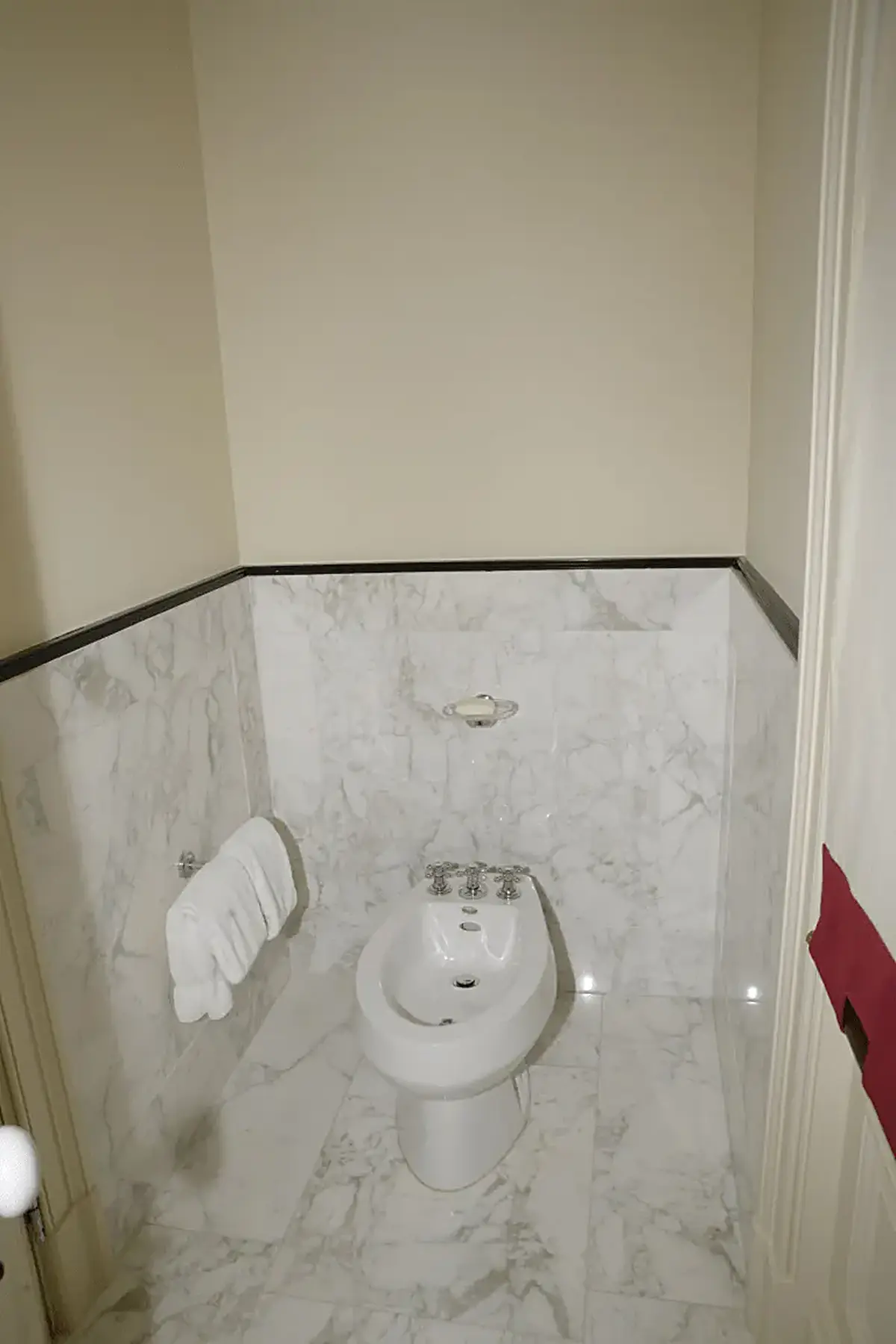 Bathroom: EFTA00000241 - White bidet in a marble-walled bathroom with folded towels on the wall and