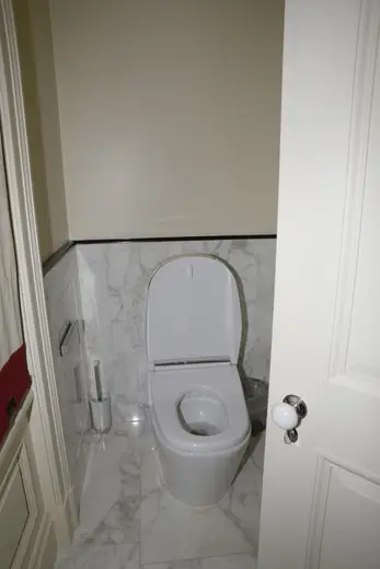 Bagno: EFTA00000242 - White toilet in a small bathroom with marble tiles a trash can and a door p