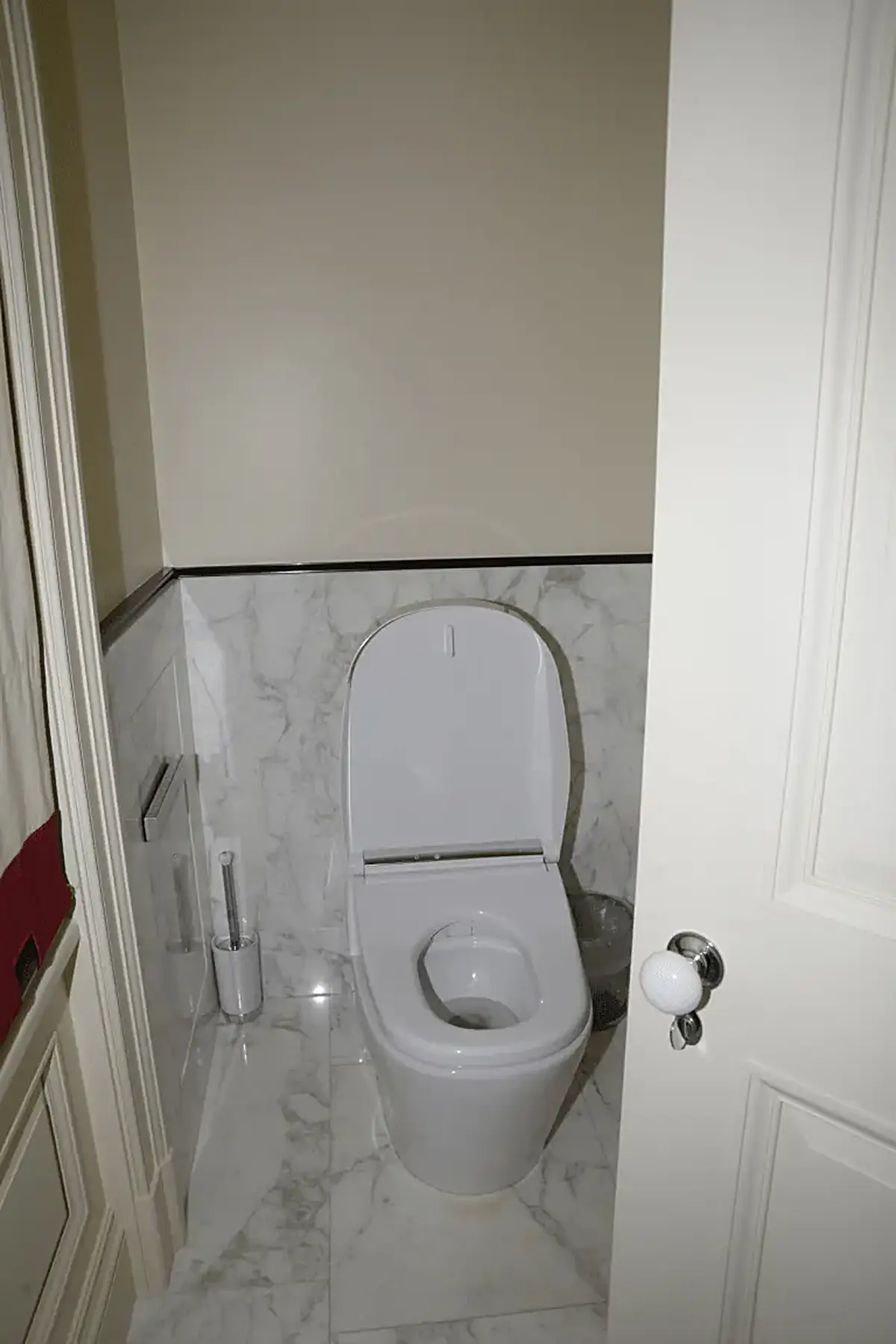 Bathroom: EFTA00000242 - White toilet in a small bathroom with marble tiles a trash can and a door p