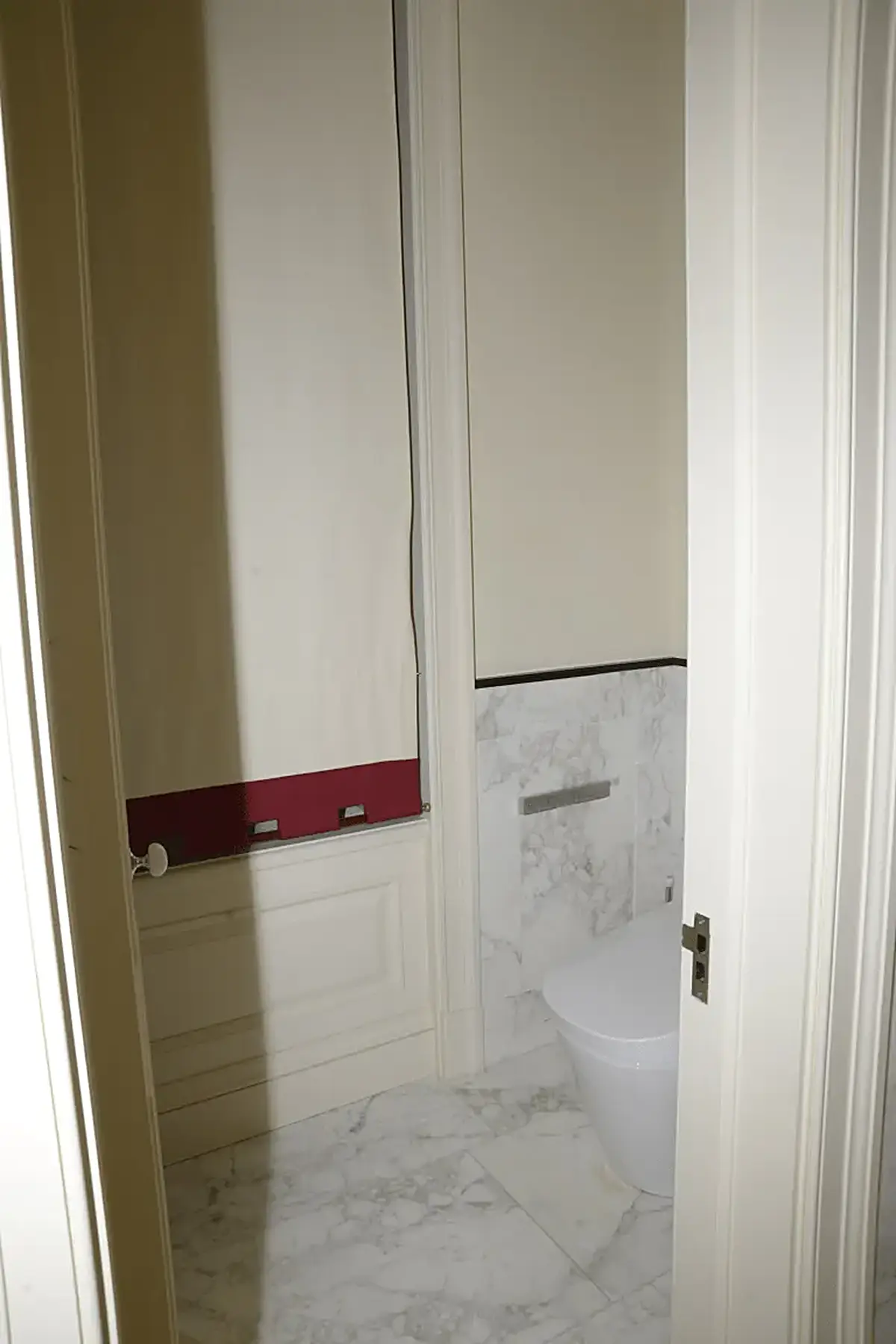 Bathroom: EFTA00000604 - Bathroom with white marble flooring a modern toilet and a red trim on the w