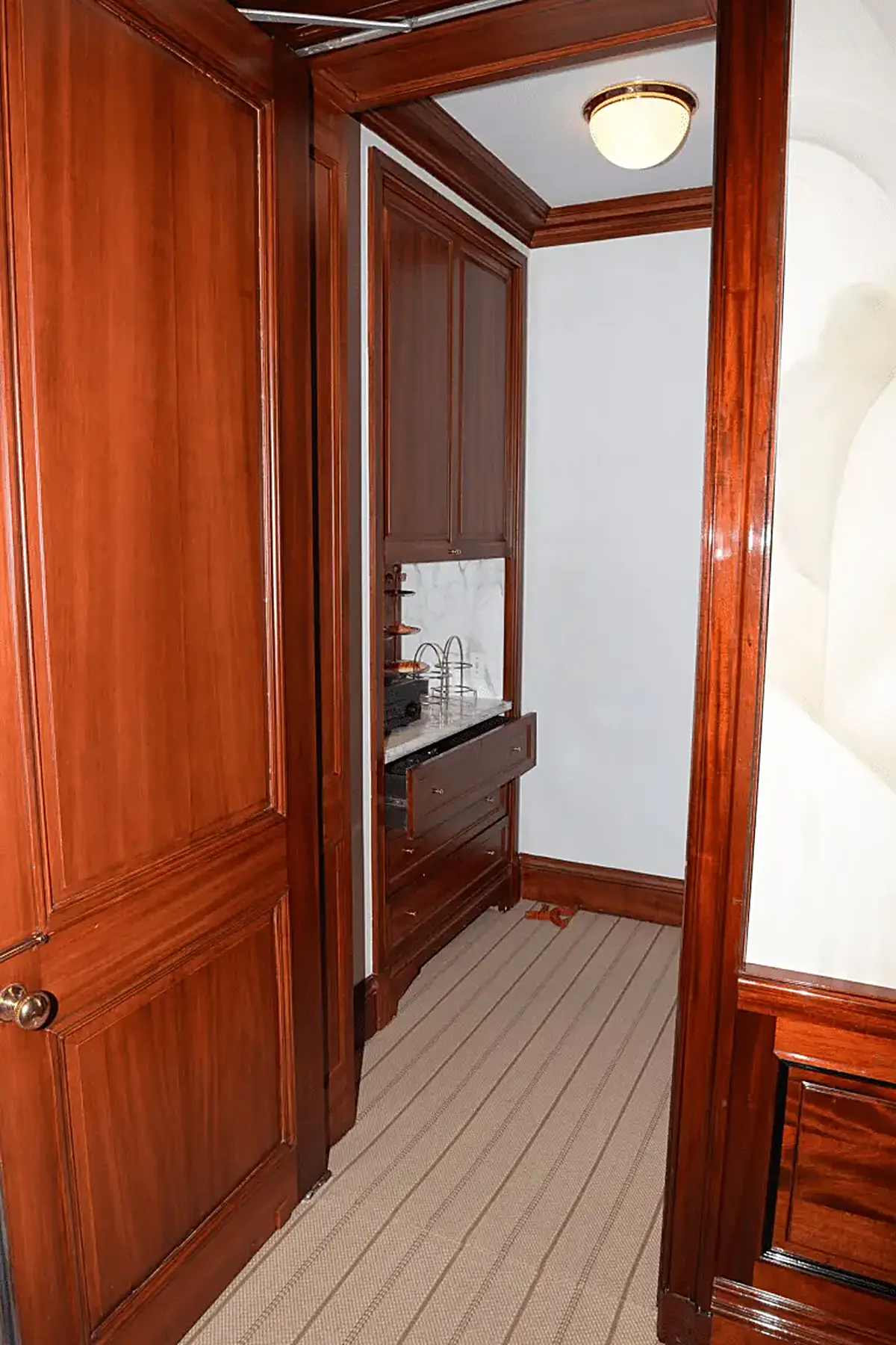 Bathroom: EFTA00001452 - Wooden hallway leads to a small bathroom with a marble countertop drawers a