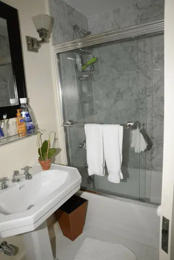 Bagno: EFTA00000296 - Bathroom with a white pedestal sink marble-tiled walls a glass shower enclo