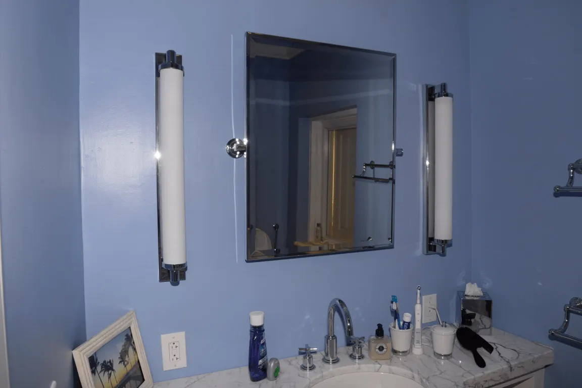 Bathroom: EFTA00001792 - Bathroom with blue walls a marble countertop and a mirror flanked by two wh