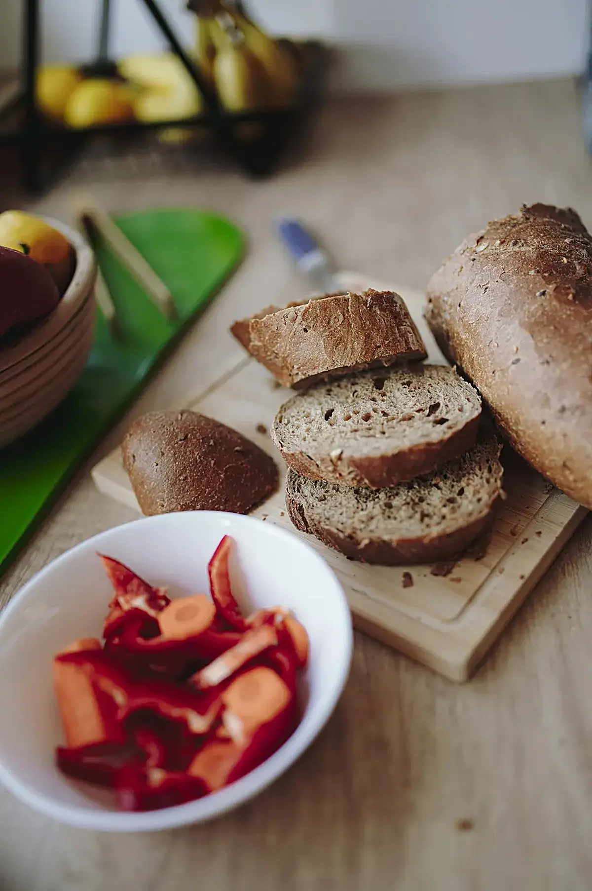 Kitchen: Freshly sliced bread alongside colorful vegetable slices on a wooden countertop in a kitch