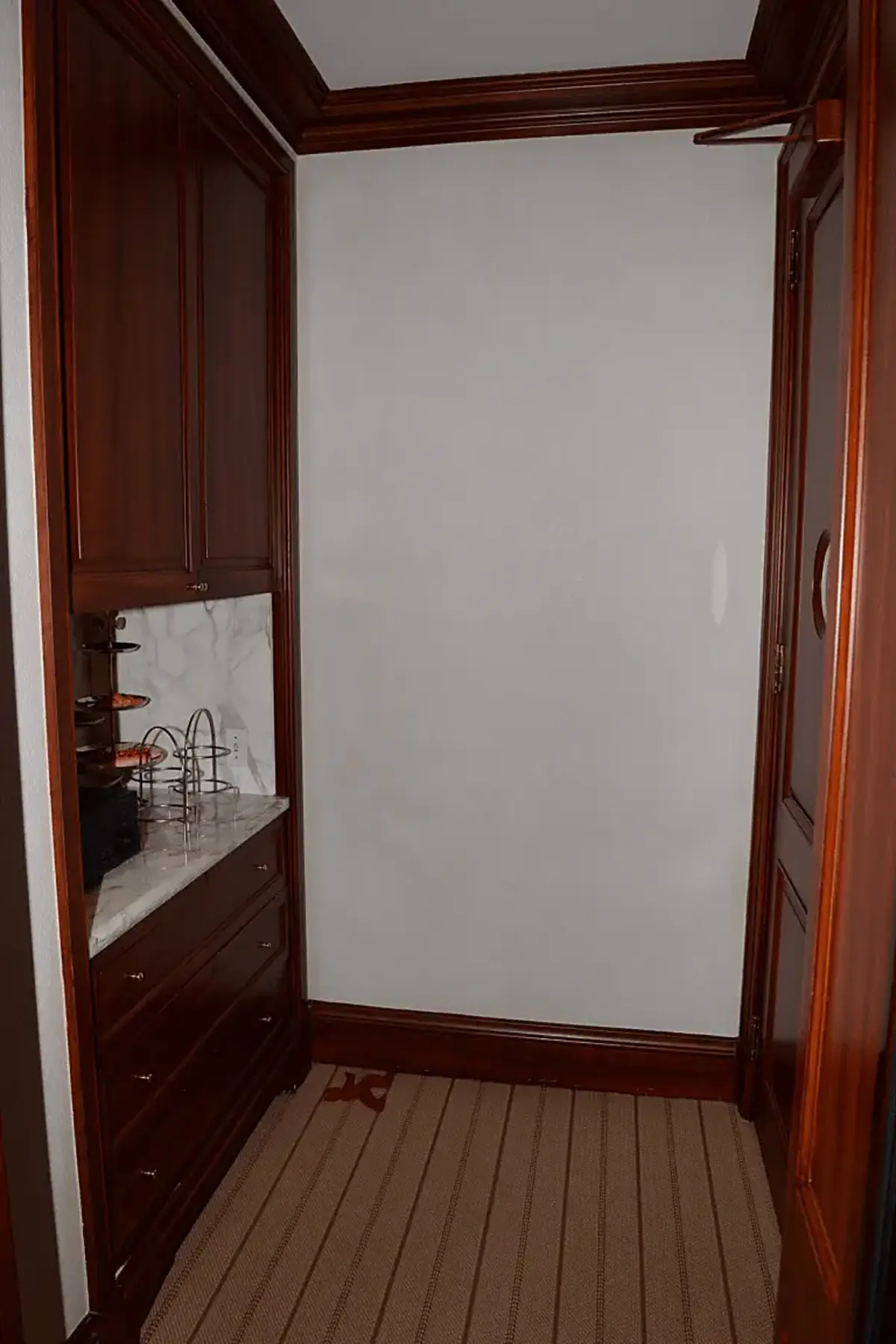 Kitchen: EFTA00000952 - Narrow hallway with dark wood cabinetry a marble countertop and striped car