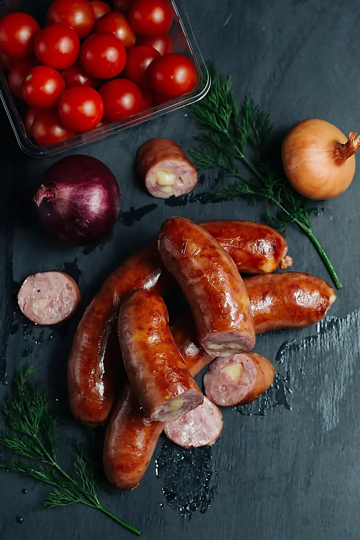 Cucina: Sausages surrounded by fresh vegetables on a dark countertop ready for preparation