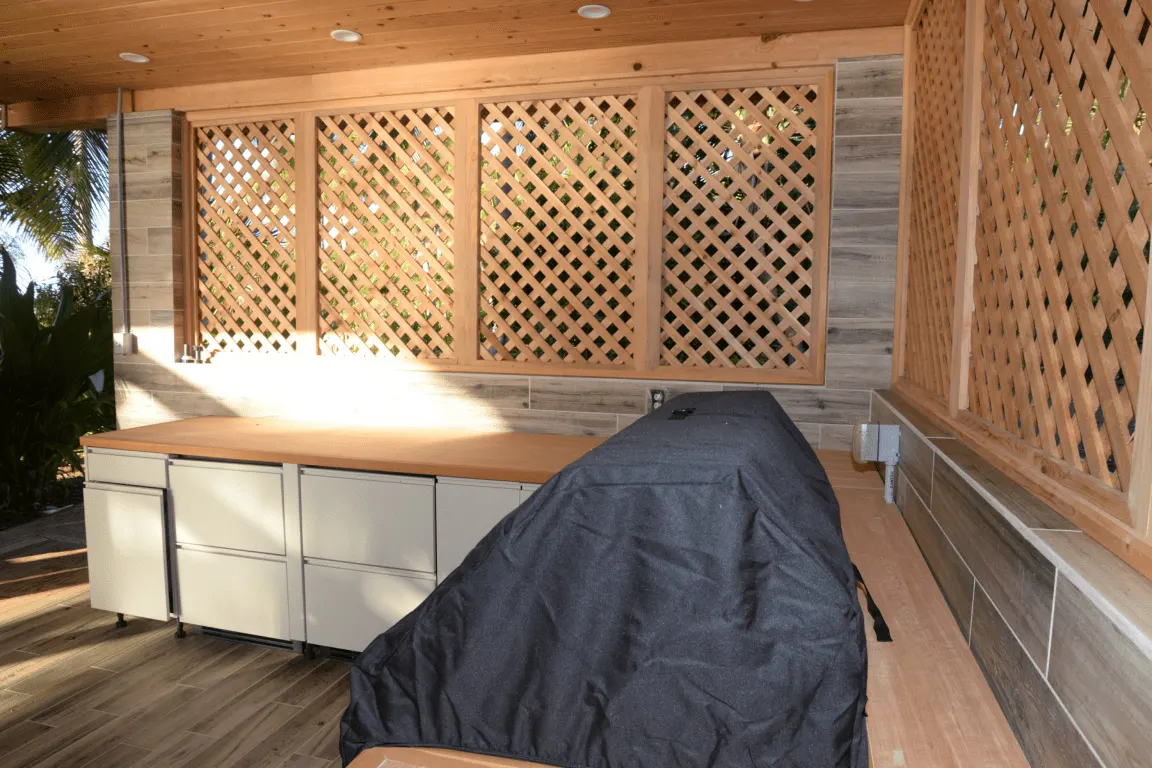 Кухня: EFTA00002811 - Wooden lattice wall and countertop surround a covered grill in a sunny outd