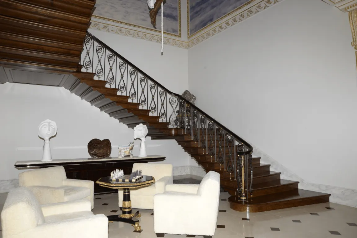 Scala: EFTA00000053 - Grand wooden staircase with intricate iron railings ascends flanked by whit