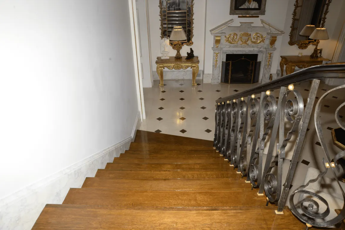 Escalera: EFTA00000822 - Grand wooden staircase leads to an opulent hallway featuring ornate iron ra